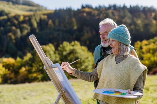 Senior couple painting surrounded autumn nature.