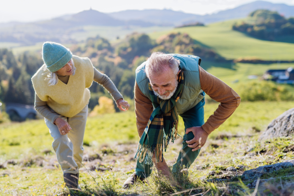 Senior man having painful knee during autumn walk, his wife taking care of him.