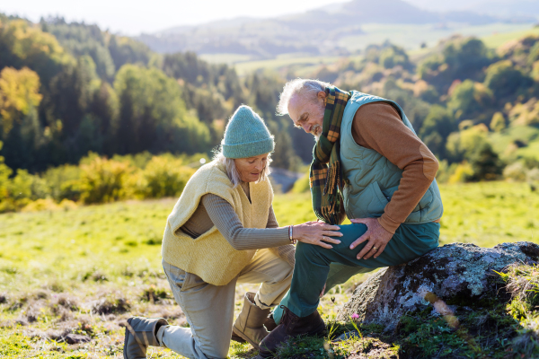 Senior man with painful knee resting during autumn walk, his wife taking care of him.