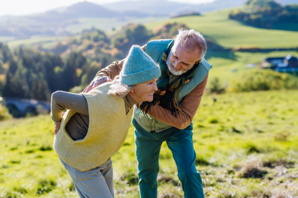 Senior woman with having pain in the back during autumn walk, her husband taking care of her.