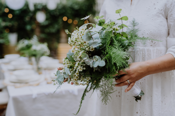 A close-up of wedding bouquet in bride's hands at reception outside in backyard