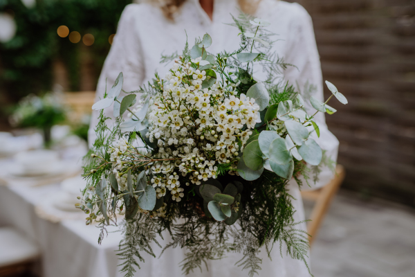 A close-up of wedding bouquet in bride's hands at reception outside in backyard