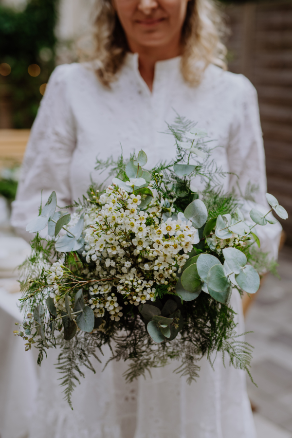 A close-up ofwedding bouquet in bride's hands at reception outside in backyard