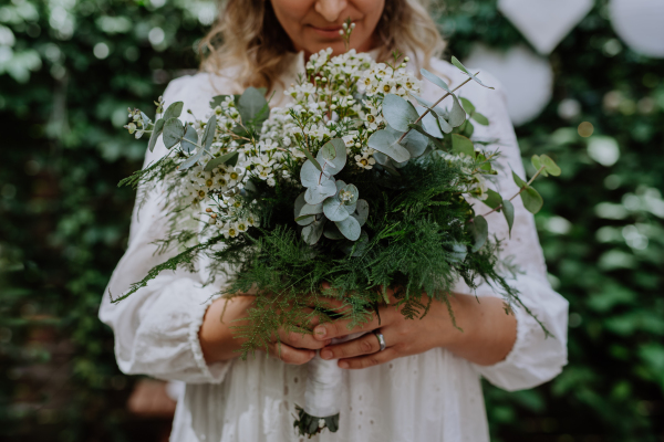 A close-up ofwedding bouquet in bride's hands at reception outside in backyard