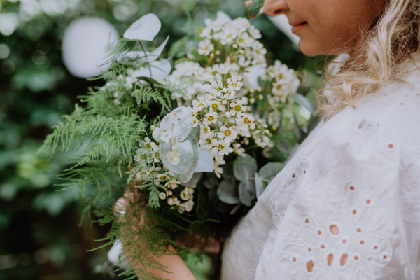 A close-up of wedding bouquet in bride's hands at reception outside in backyard