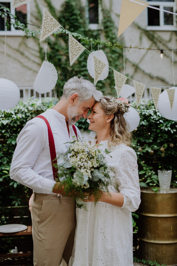 A mature bride and groom having a romantic moment at wedding reception outside in the backyard.