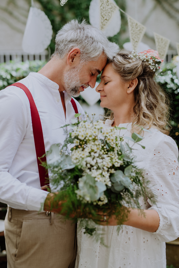 A mature bride and groom having a romantic moment at wedding reception outside in the backyard.