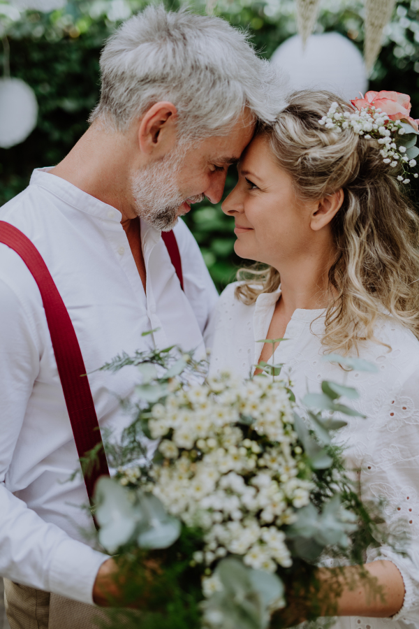 A mature bride and groom having a romantic moment at wedding reception outside in the backyard.