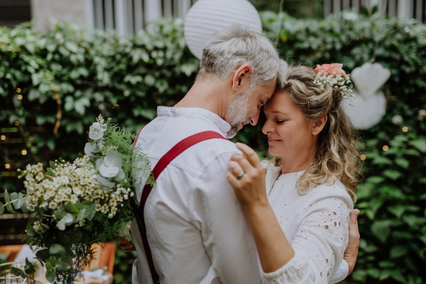 A mature bride and groom having a romantic moment at wedding reception outside in the backyard.