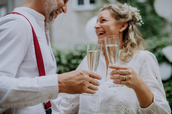 A mature bride and groom toasting at wedding reception outside in the backyard.