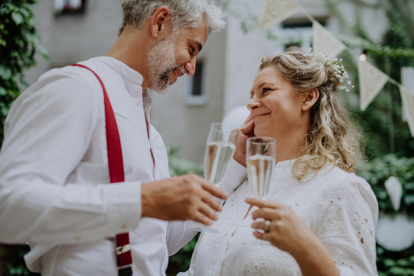 A mature bride and groom toasting at wedding reception outside in the backyard.