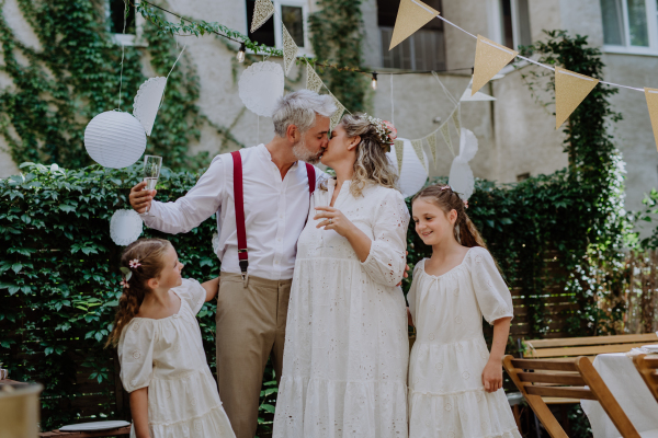 Mature bride and groom toasting with their daughters at wedding reception outside in backyard.