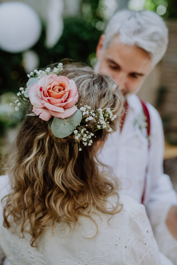 A mature groom recieving decoration on his shirt from bride at wedding reception outside in the backyard.