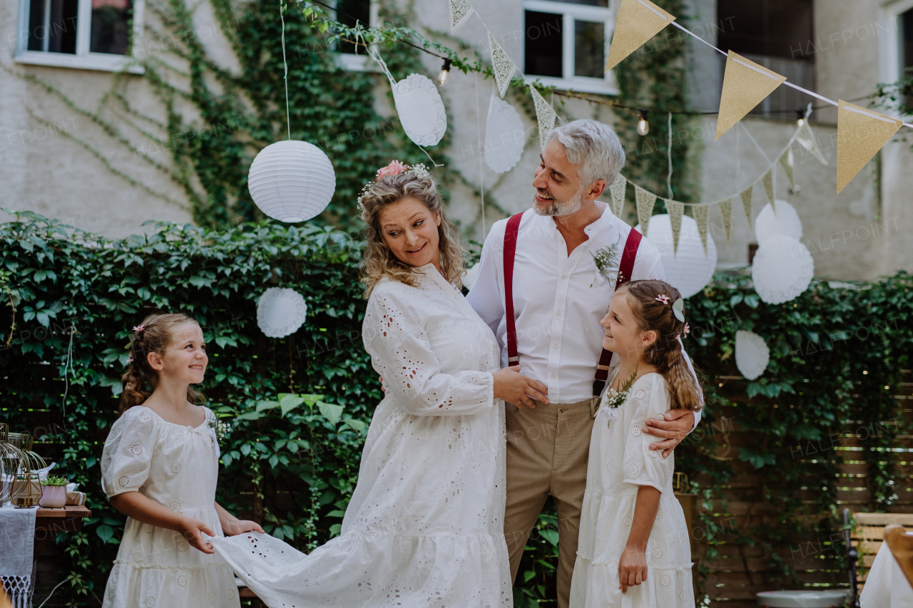 Little daughter holding a wedding dress train her mother at backyard party.