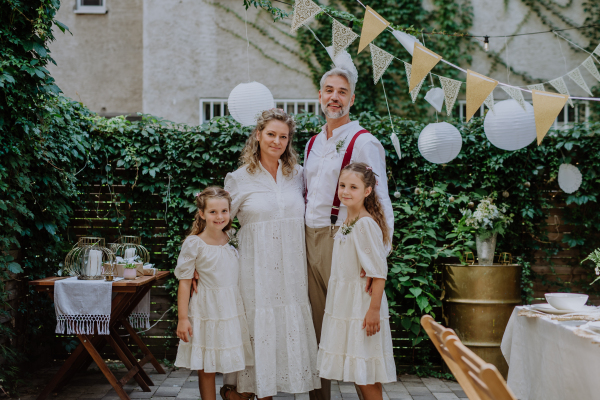 Mature bride and groom posing with their daughters at wedding reception outside in backyard.