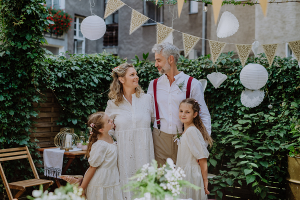 Mature bride and groom posing with their daughters at wedding reception outside in backyard.