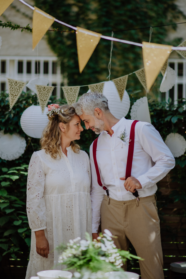 A mature bride and groom having a romantic moment at wedding reception outside in the backyard.