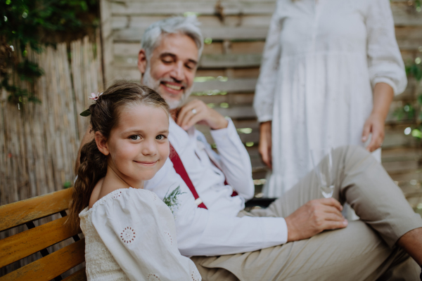 Little girl sitting with groom at an outdoor wedding party.