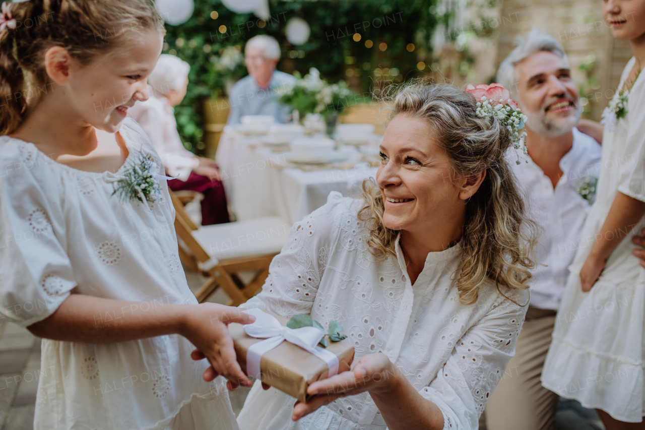 Little girl giving a wedding gift to mature bride at wedding backyard party.