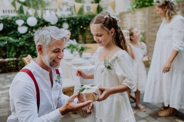 A mature father groom receiving gift from his daughter at wedding reception outside in the backyard.