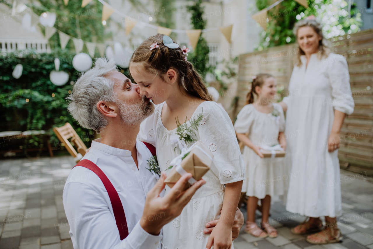 A mature father groom receiving gift from his daughter at wedding reception outside in the backyard.