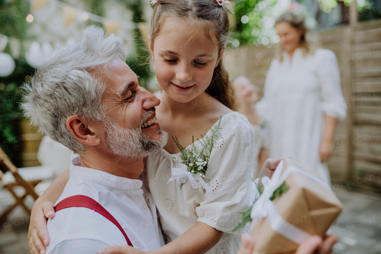 A mature father groom receiving gift from his daughter at wedding reception outside in the backyard.