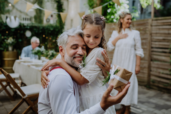 A mature father groom receiving gift from his daughter at wedding reception outside in the backyard.