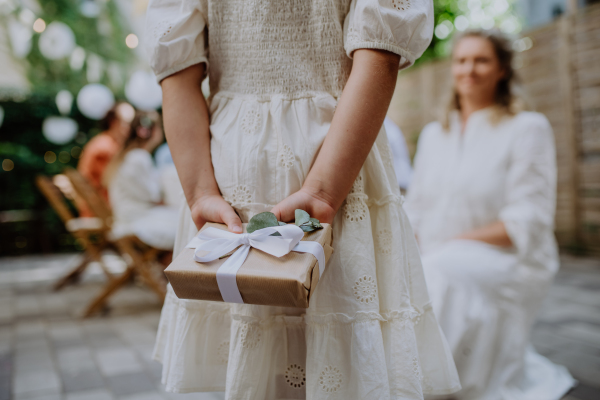 Rear view of little child giving wedding gift to mature bride at a wedding backyard party.