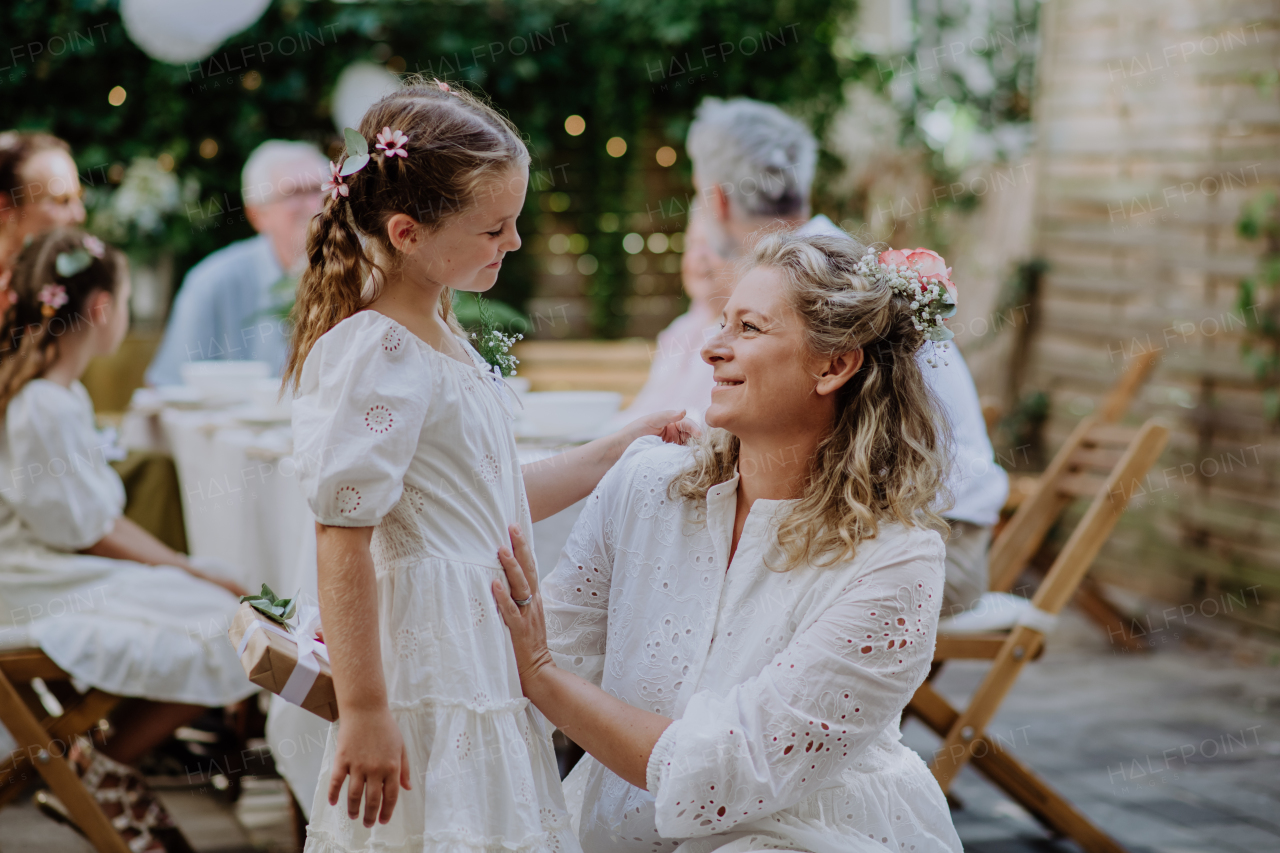 Little girl giving a wedding gift to mature bride at wedding backyard party.