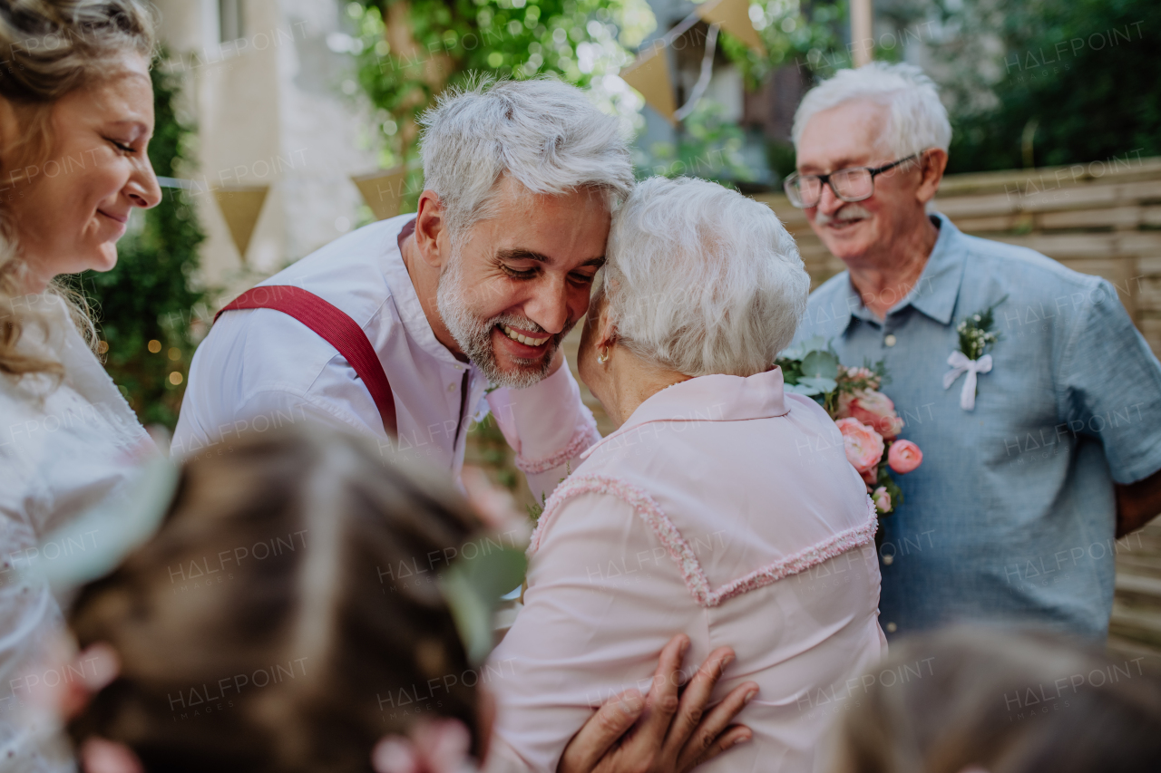 A mature bride and groom receiving congratulations at wedding reception outside in the backyard.