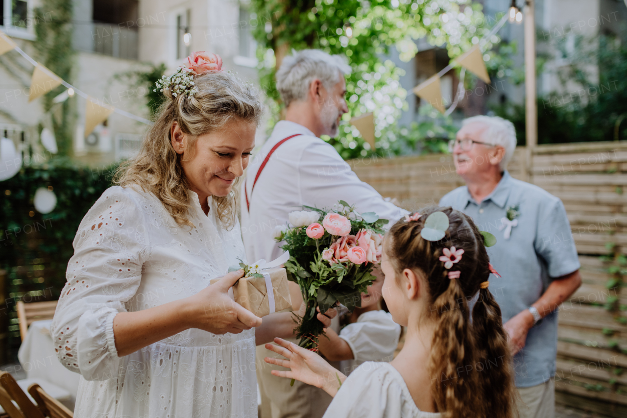 Little girl giving a wedding gift to mature bride at wedding backyard party.