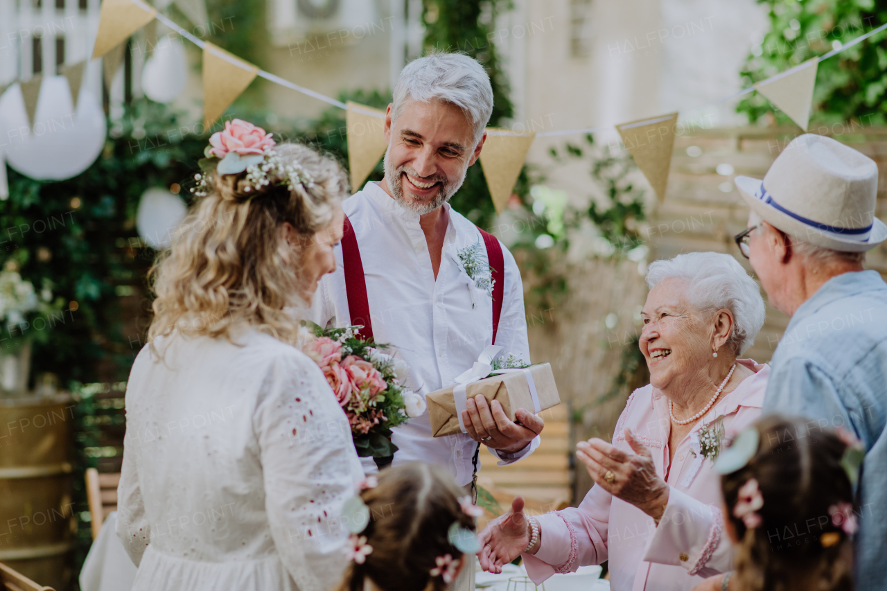 A mature bride and groom receiving congratulations at wedding reception outside in the backyard.