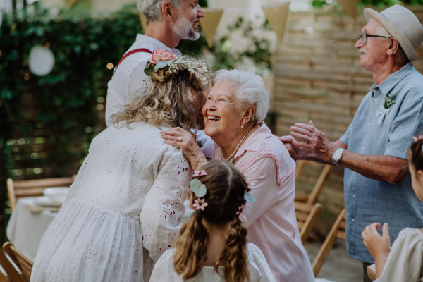 A mature bride and groom receiving congratulations at wedding reception outside in the backyard.