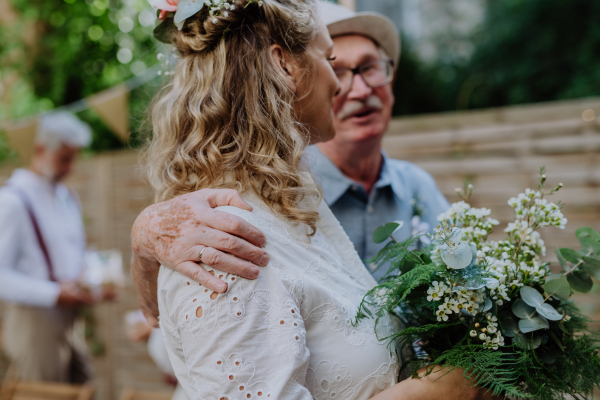 A mature bride receiving congratulations at wedding reception outside in the backyard.