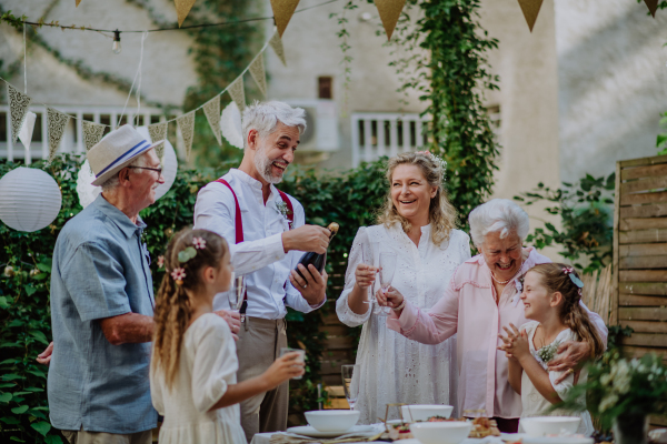 A mature bride and groom toasting with guests at wedding reception outside in the backyard.