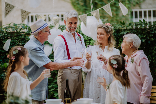 A mature bride and groom toasting with guests at wedding reception outside in the backyard.