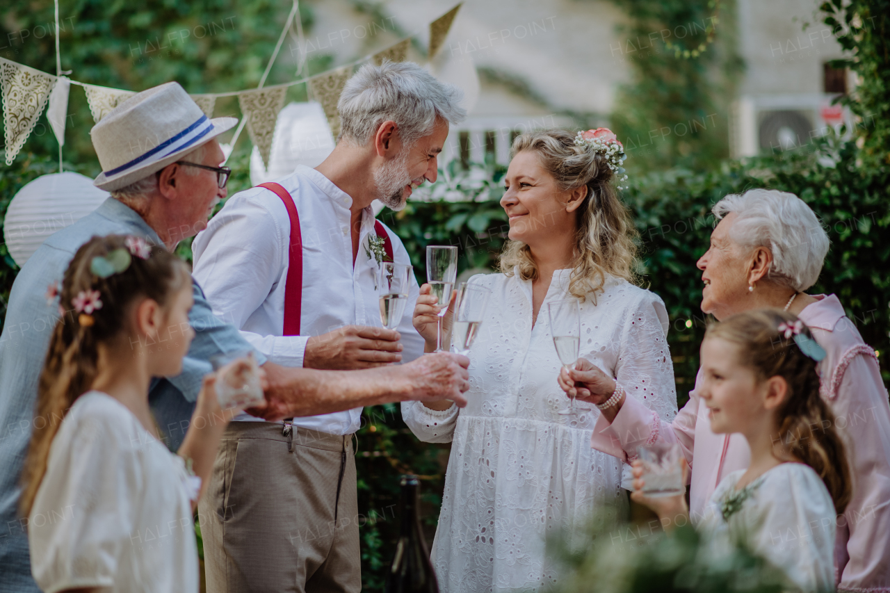 A mature bride and groom toasting with guests at wedding reception outside in the backyard.