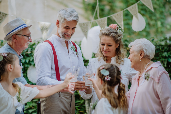 A mature bride and groom toasting with guests at wedding reception outside in the backyard.