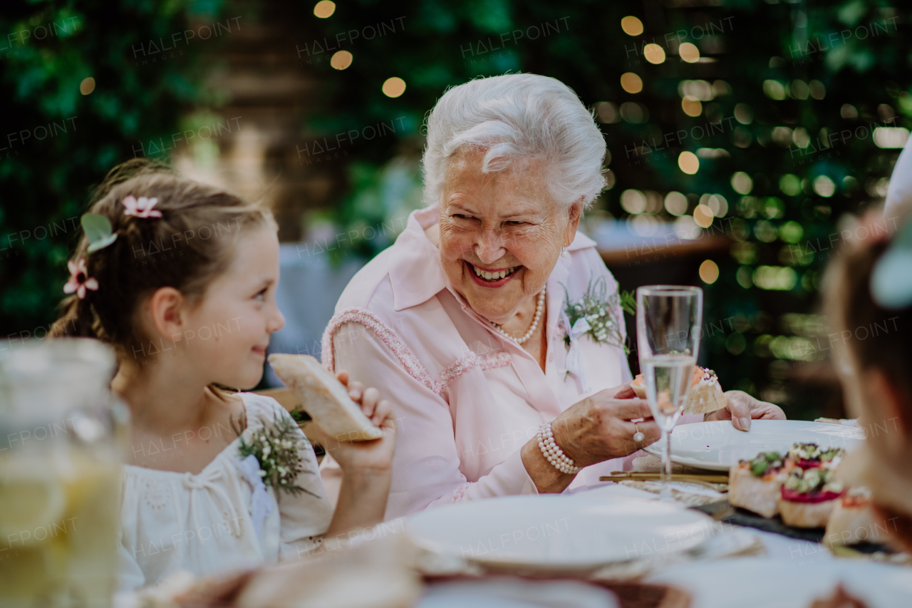 Wedding guests sitting by table, eating and drinking at a reception outside in the backyard.