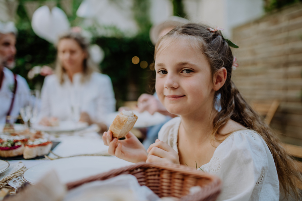 Wedding guests sitting by table, eating and drinking at a reception outside in the backyard.