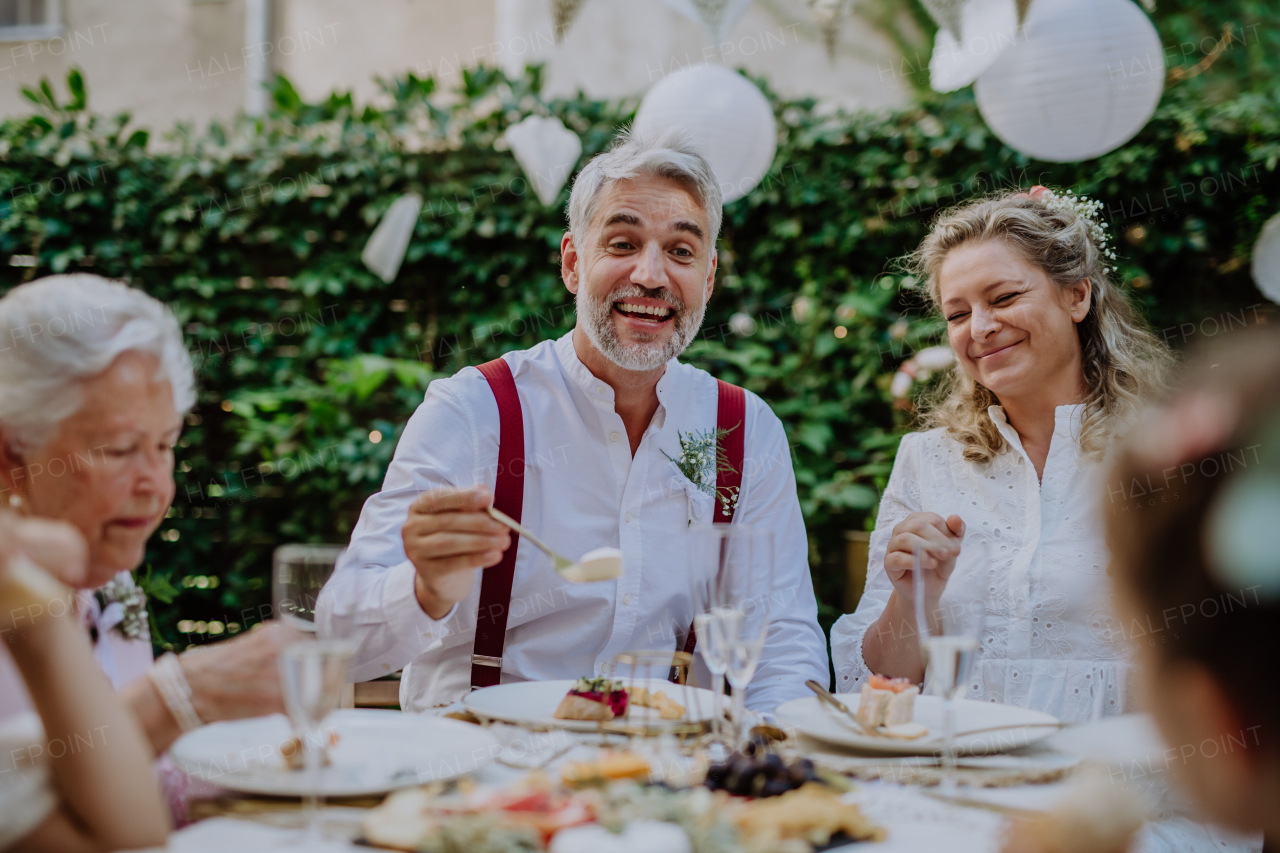 A mature bride and groom with guests at wedding reception outside in the backyard.