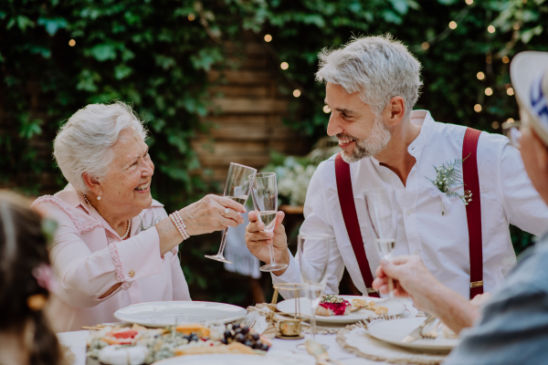 Mature groom toasting with his mother in law at wedding reception outside in backyard.