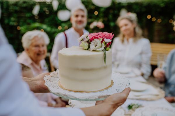 A mature bride and groom getting a cake at wedding reception outside in the backyard.