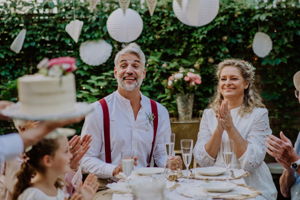 A mature bride and groom with guests at wedding reception outside in the backyard.