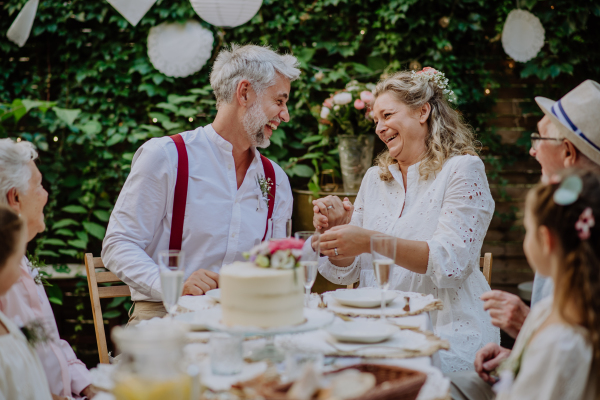 A mature bride and groom with guests at wedding reception outside in the backyard.