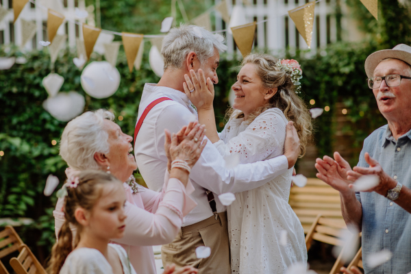 Mature bride and groom celebrating marriage with their family, outside in a backyard.