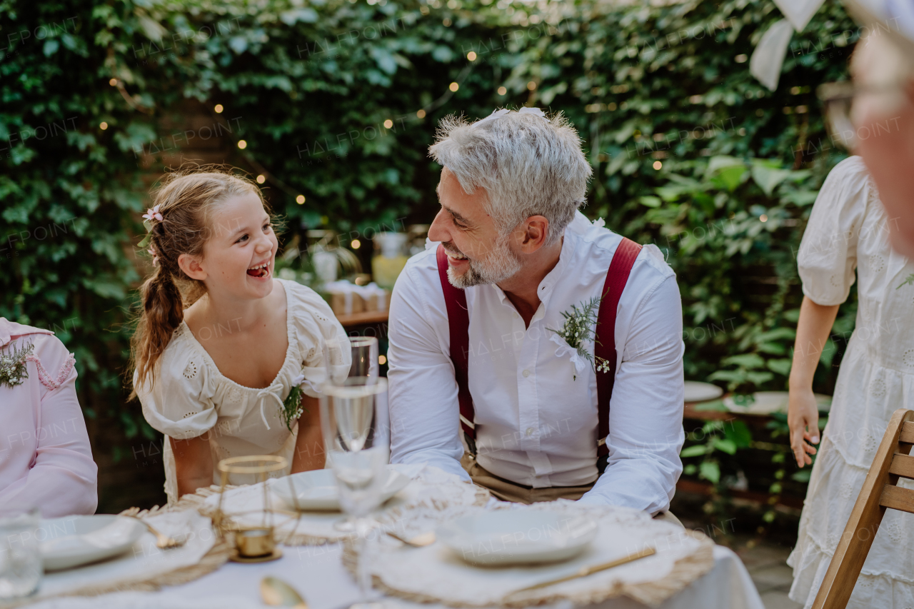 Happy groom talking and smiling with his little daughter during garden wedding party.