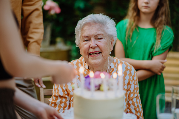 Celebration of grandmother birthday, outdoor family garden party with a cake with candles.