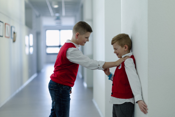 A frightened schoolboy being bullied by classmate in school corridor