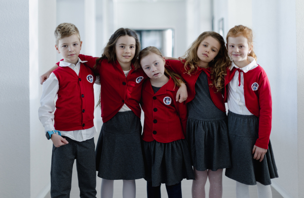 Happy schoolgrirl with Down syndrome standing with classmates in school corridor, looking at camera.